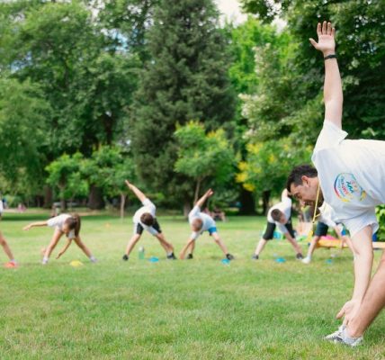 Kids stretching exercises in a park guided by a coach, promoting fitness and fun.