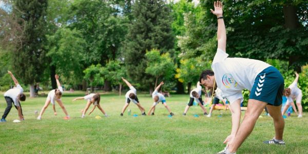 Kids stretching exercises in a park guided by a coach, promoting fitness and fun.