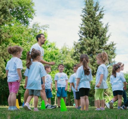 Group of children and teachers playing and learning in a sunny park setting.