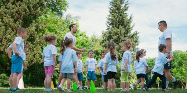 Group of children and teachers playing and learning in a sunny park setting.