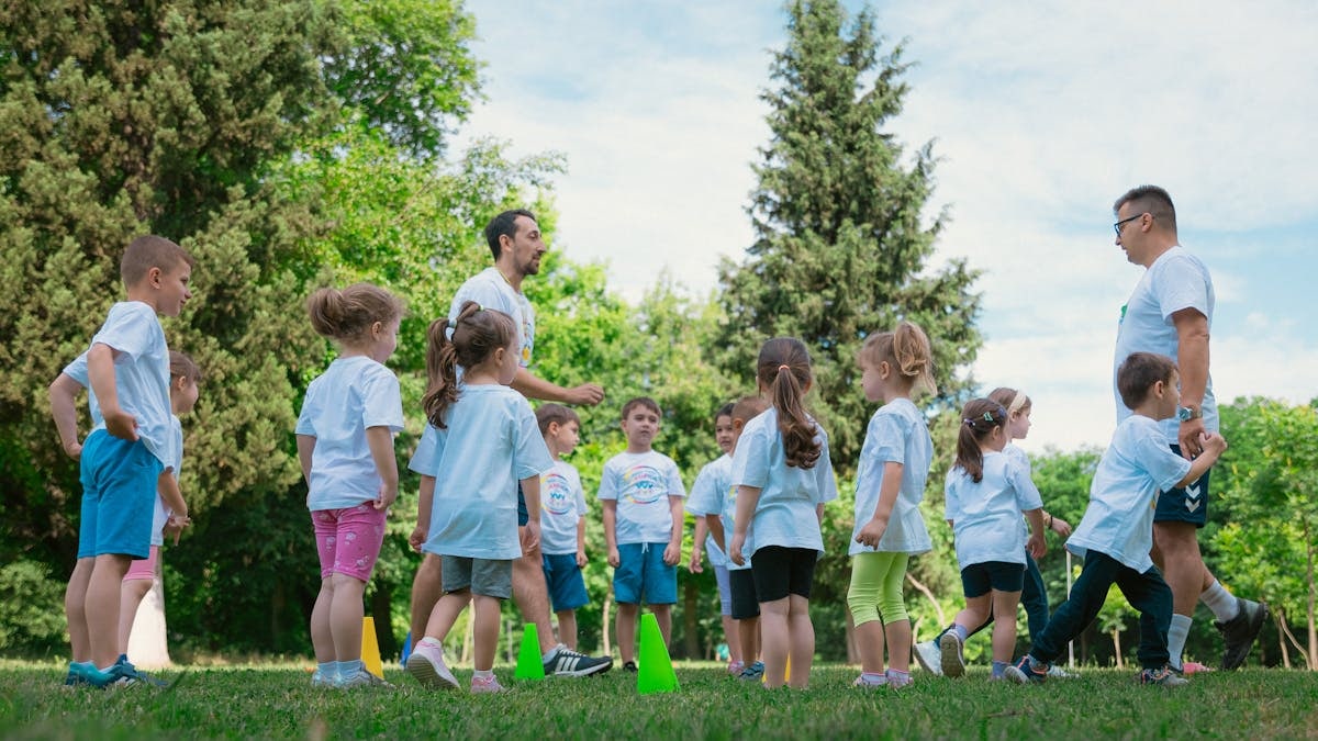 Group of children and teachers playing and learning in a sunny park setting.