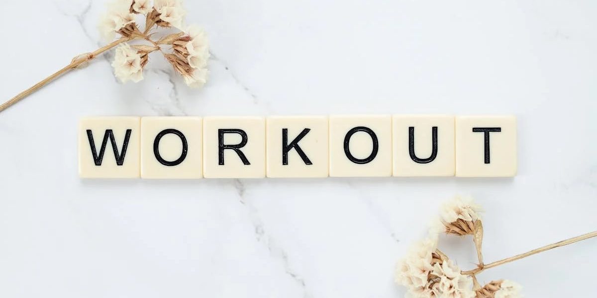 Letter tiles spelling 'WORKOUT' on marble with dried flowers, conveying fitness motivation.