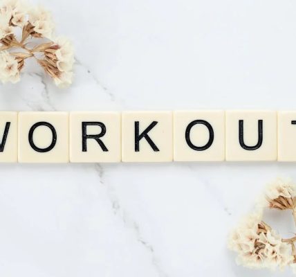 Letter tiles spelling 'WORKOUT' on marble with dried flowers, conveying fitness motivation.